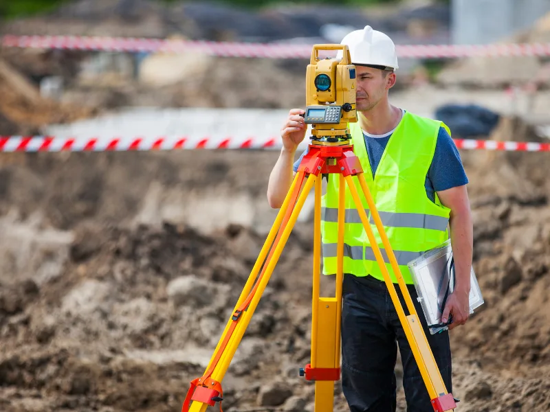 Survey technician collecting site measurements with surveying equipment at a construction project
