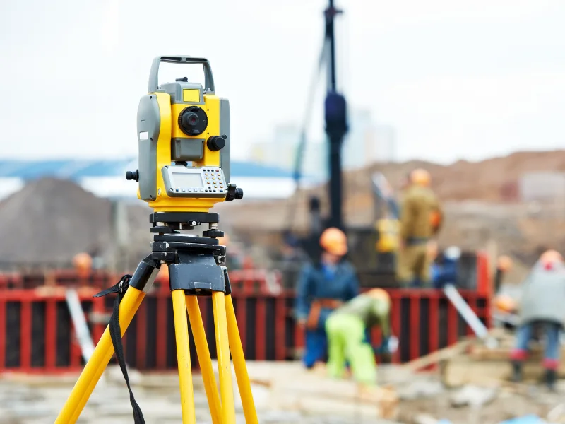Yellow total station used for land surveying at an active construction site