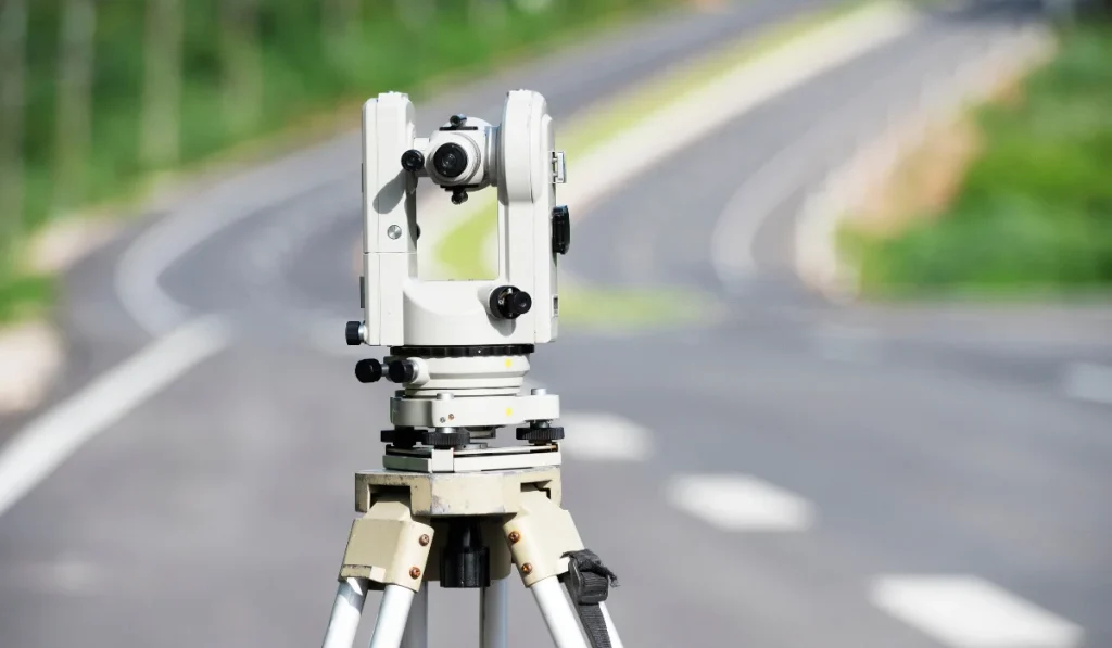 Surveying instrument set on a tripod positioned on a road for land measurement and alignment.
